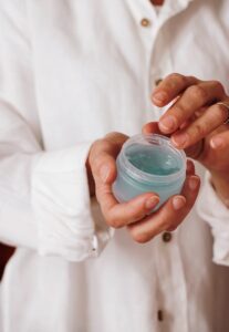 person holding blue plastic container of a skincare product