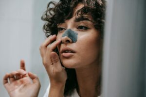 Mirror reflection of young female with curly hair putting nose strip mask on face in bathroom |Unclog Pores and prevent blackheads