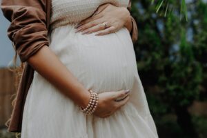 A pregnant woman wearing a white dress and holding her belly | Pregnancy-Safe Nail Polish