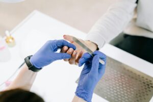 A Person in Blue Gloves Holding a Nail File And Using it to Her Client