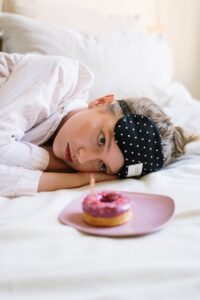 Young woman resting with an eye mask, gazing at a donut on a plate. | Skin Fast