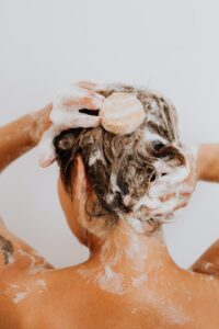 Close-up of a woman washing her hair with soap and lather in the shower.