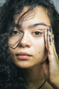 Close-up portrait of a young woman with painted hands, highlighting artistic expression. | Pre-Poo