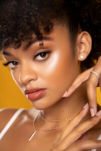 Close-up portrait of a young woman with curly hair, posing elegantly against a yellow background.