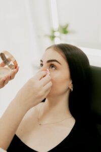 Close-up of a makeup artist applying powder to a woman's face indoors.