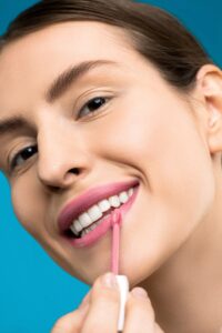 Smiling woman applying pink lipstick, showcasing beauty and makeup.