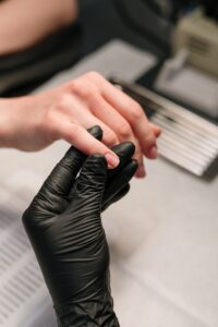 A professional manicurist wearing black gloves provides a manicure service to a client.