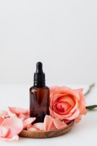 Elegant dropper bottle with pink rose petals on a wooden plate, perfect for aromatherapy or skincare.