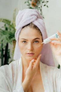 Woman with head towel applying moisturizer, showcasing a skincare routine.