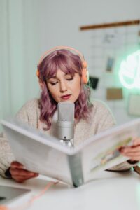 Woman podcasting indoors, reading from a book with microphone and headphones. | Confidence Podcast