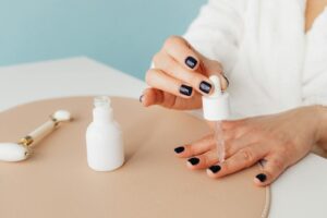 Close-up of a woman applying nail oil with a dropper for manicure care on blue background. | Cuticle Oil