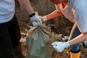 Two people tying a sack of garbage during an outdoor community cleanup activity.