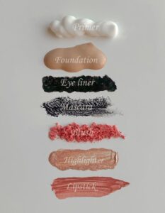 Stylish flat lay of cosmetics swatches including primer, foundation, eyeliner, mascara, blush, highlighter, and lipstick.