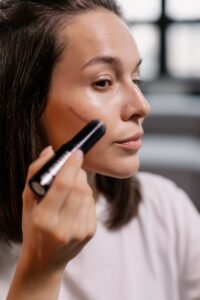 Close-up of a woman applying contour makeup with a cosmetic stick indoors.