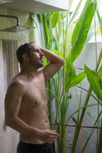 A man standing in a shower next to a bamboo plant