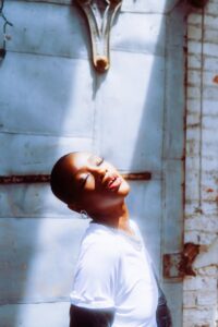 Artistic portrait of a woman basking in sunlight against a rustic urban backdrop.