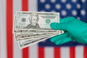 A gloved hand holds US dollar bills against an American flag, symbolizing finance and protection.