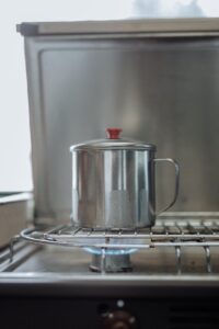 An indoor shot of a stainless steel kettle boiling on a gas stove with visible flame.