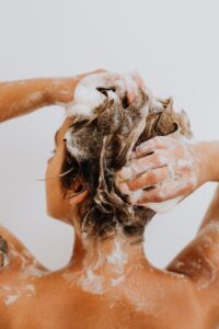 Back view of a woman washing her hair in a shower with white background.