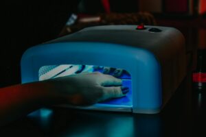 A hand with manicured nails being cured under a blue LED lamp for gel polish | Nail Technician Essentials