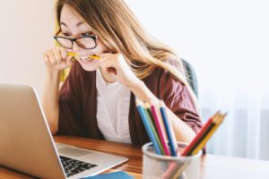 woman biting pencil while sitting on chair in front of computer during daytime | Cosmetology State Board Exam