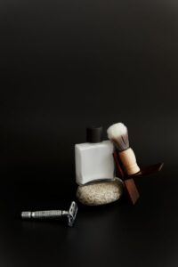 Sophisticated still life of shaving kit with razor, brush, and bottle on a black background.