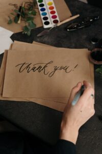 Artist hand crafting a thank you card with calligraphy on brown paper.