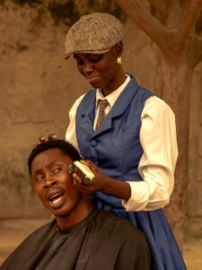 Barber skillfully giving a haircut to a client outdoors in a warm environment.