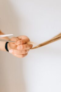 Detailed close-up of a hand holding hair while cutting with scissors against a white background.