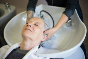 Senior woman relaxing during a hair wash at a salon. The hairstylist gently massages her hair in an inviting, serene setting | Scalp Massage