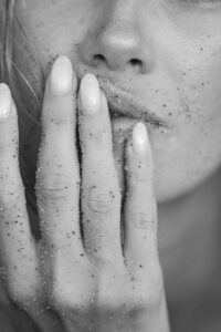 Close-up black and white image of a woman's sandy fingers touching her lips. | Natural Nails