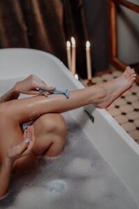 A serene bath scene with a woman shaving her legs by candlelight, highlighting relaxation and skincare.