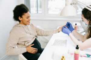A pregnant woman receives a manicure at a nail salon, highlighting self-care and beauty.