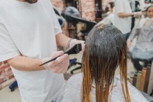 Hair coloring process in a salon, showcasing stylist applying color to client's hair. | balayage vs ombre: student learning hair painting technique