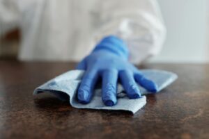 A hand wearing a blue glove wipes a surface with a cloth, emphasizing hygiene and cleanliness.