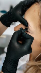 Close-up of a person receiving an eyebrow tattoo by a professional artist wearing gloves.