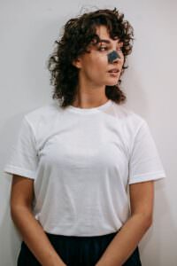Facial Treatment Basics: 6 Steps Every Esthetician Should Master 3 Young woman with curly hair using a blackhead nose strip for skincare in a white studio. | Facial treatment basics